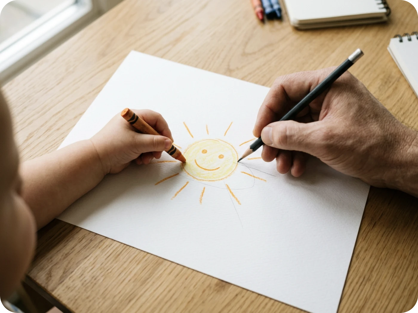 A child and a grown-up drawing a sun together at a kitchen table